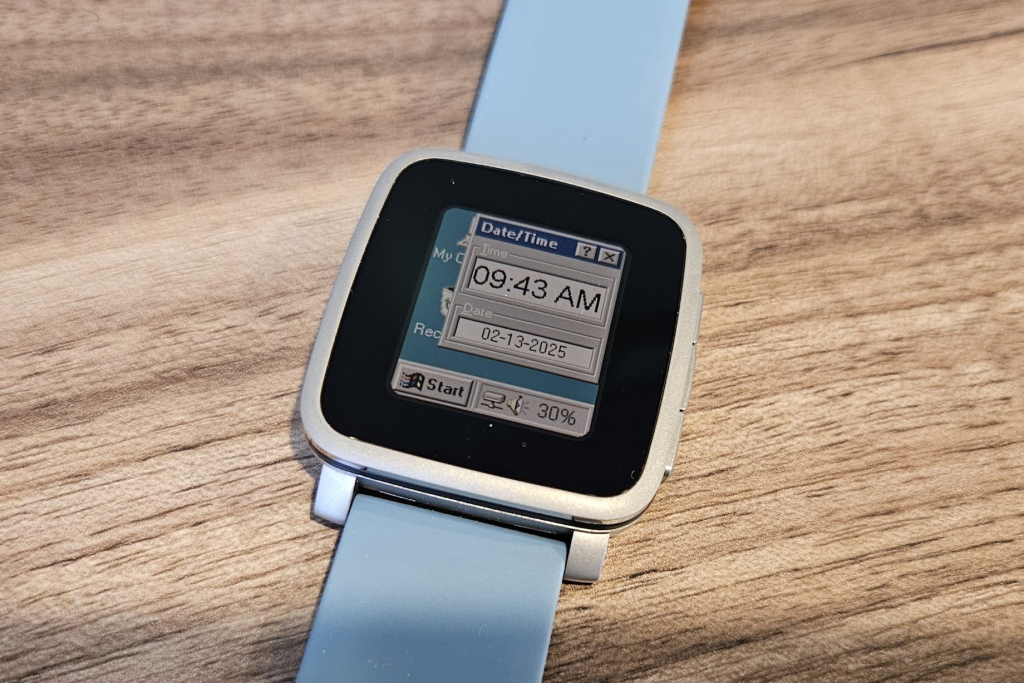 A Pebble Time Steel smartwatch with a Windows 95 watchface, including a start button over a teal background with a "Date/Time" window in the foreground.